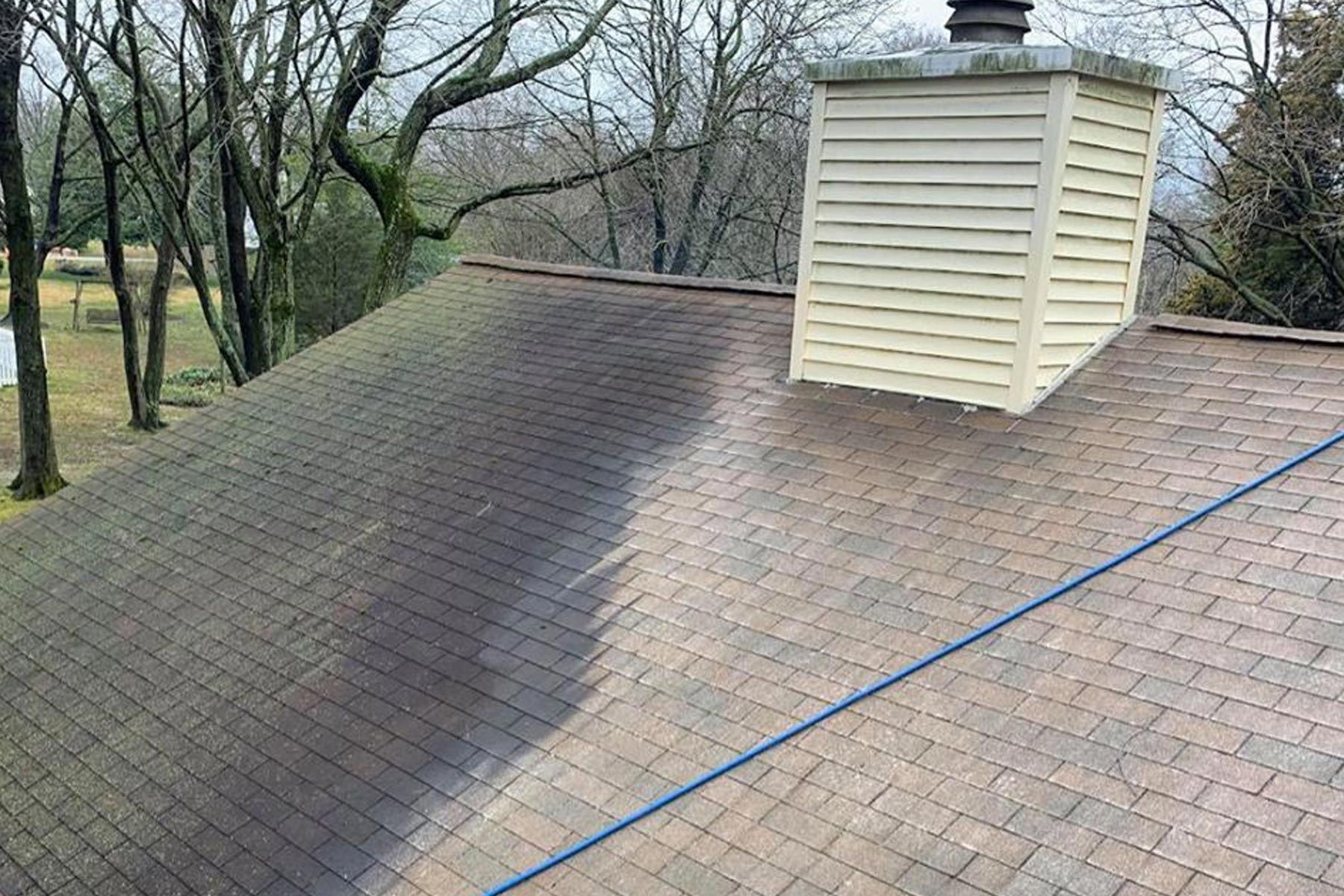 House roof partially cleaned, showing a clear contrast between clean and dirty areas with a chimney visible.